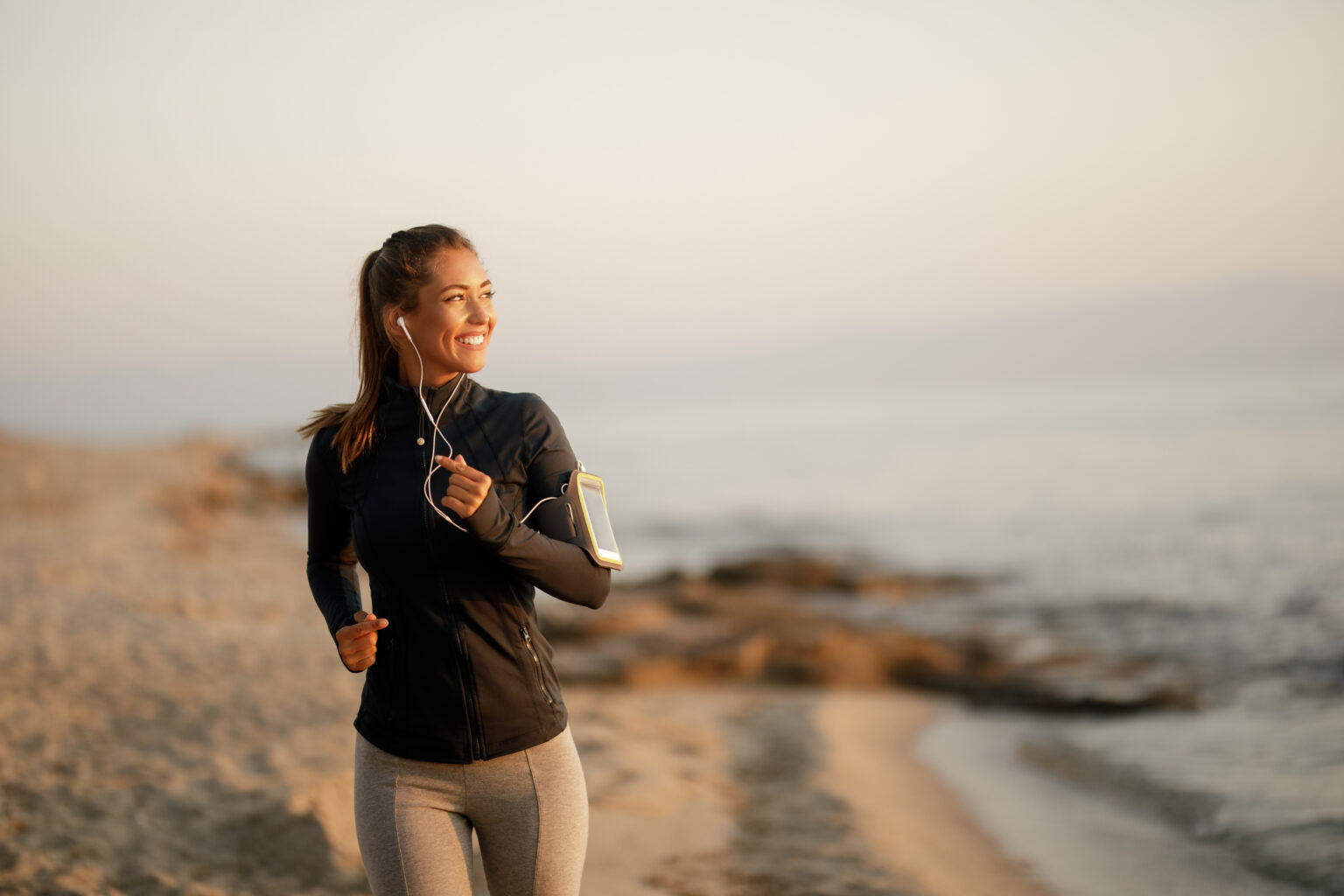 Young happy athletic woman feeling motivated while running at the beach. Copy space. hero page